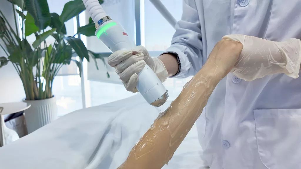 A female aesthetician performs laser hair removal on a woman on a medical couch in a beauty salon.